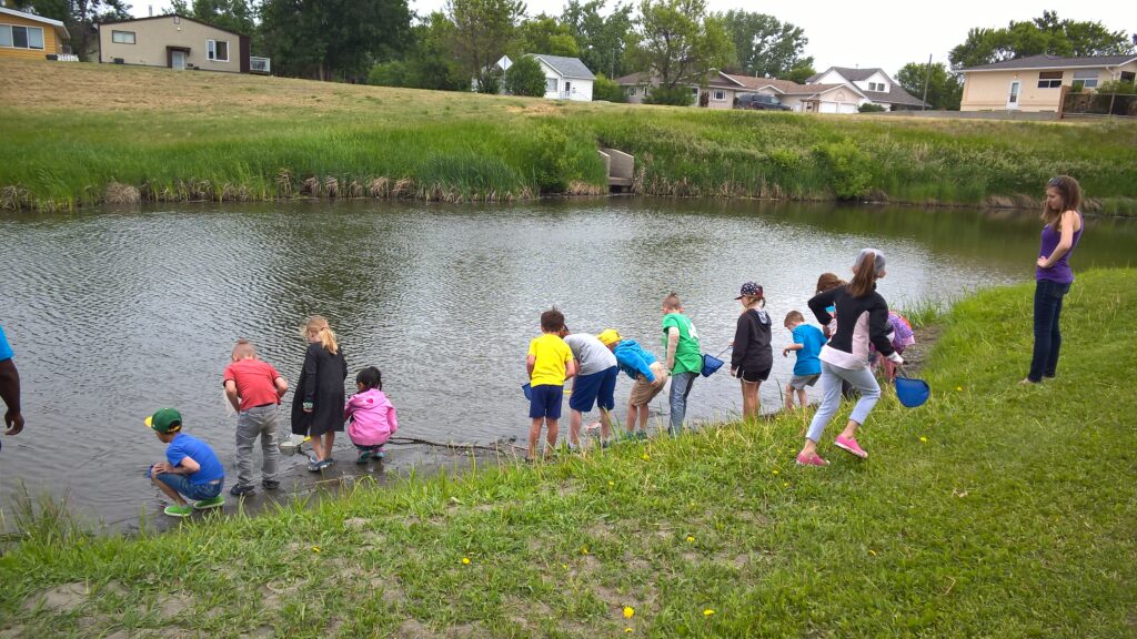 Kids examining a body of water for programming with Swift Current Nature Play