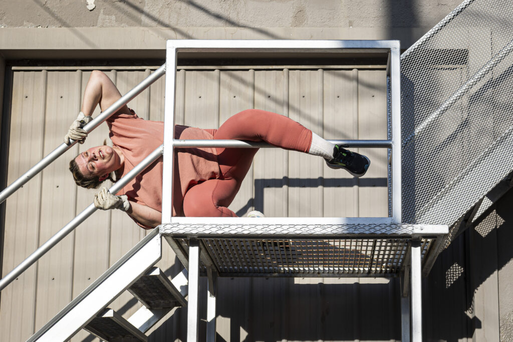 A dancer performs on a staircase in a back alley.